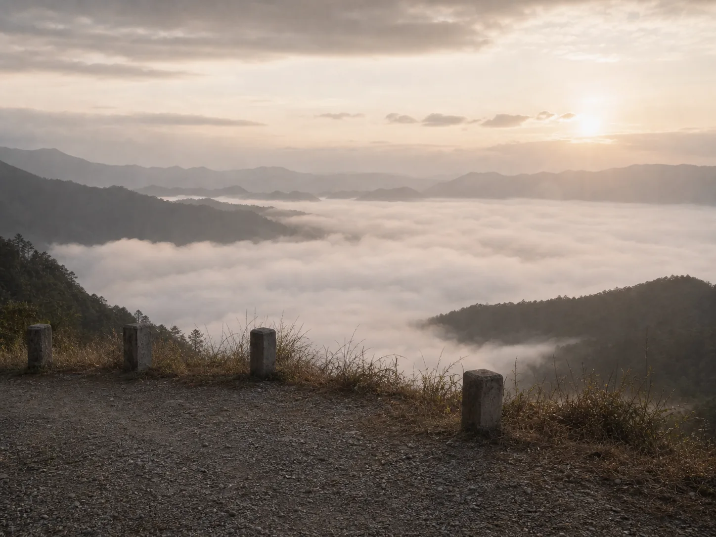 A gravel roadside pull-off facing east over a valley filled with cloud at sunrise
